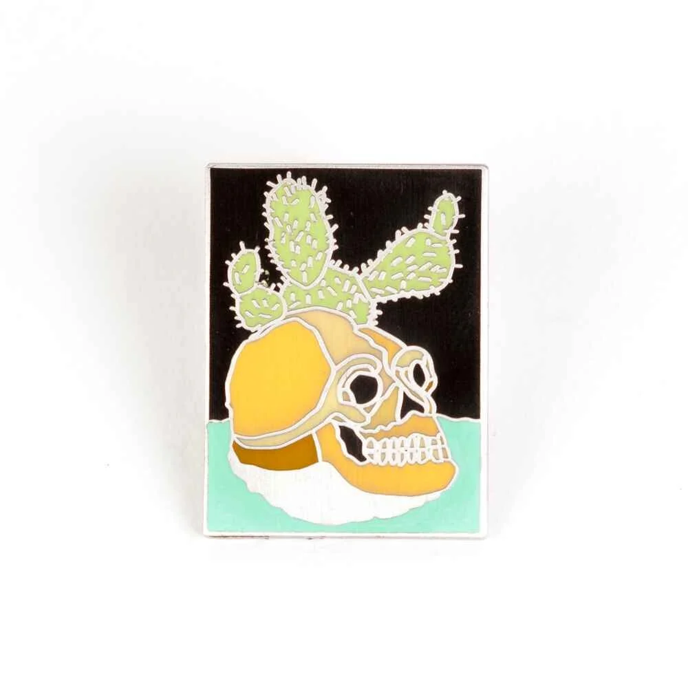 A rectangular hard enamel pin, a yellow skull with a green cactus growing through it.