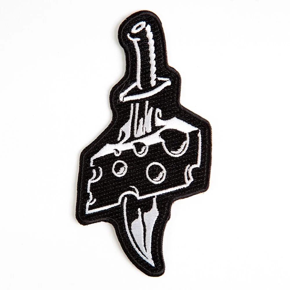 An embroidered patch cut to the shape of a knife through a wedge of cheese.
