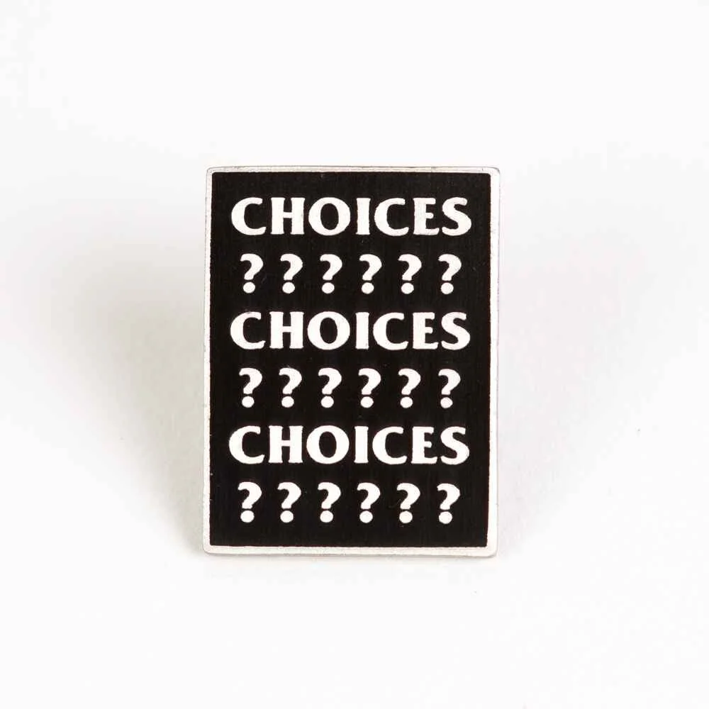 A square hard enamel pin in black and white with rows of lettering.