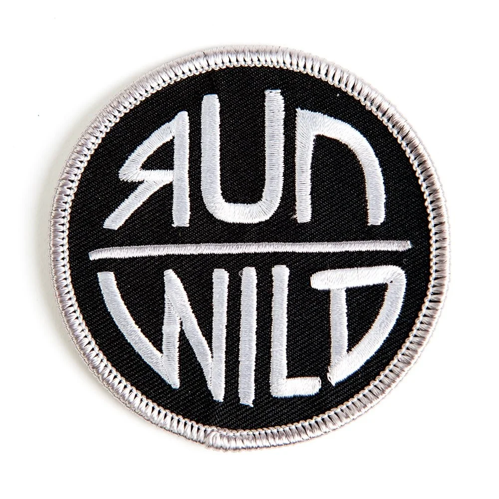 A round embroidered patch on black twill with a white merrow border.