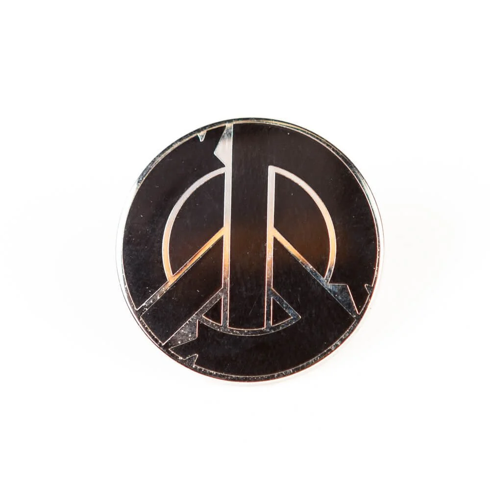 A round hard enamel pin in dark brown with a cracked peace symbol.