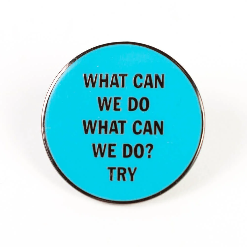 A round hard enamel pin in pale blue with lines of lettering.